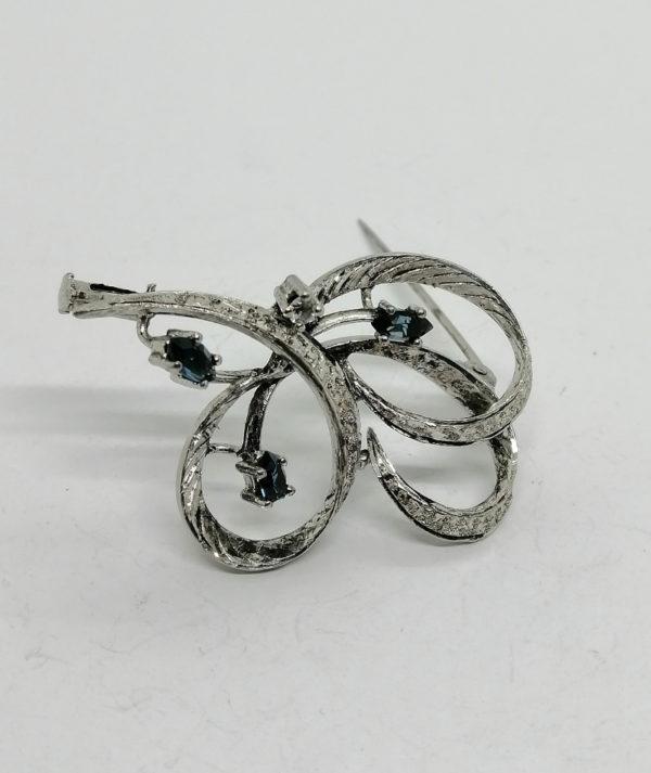 Broche argent façon ruban, ouvragée et sertie de saphirs navettes.