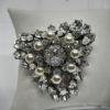 Broche/pendentif en métal blanc, avec strass en navettes et perles d'imitations.