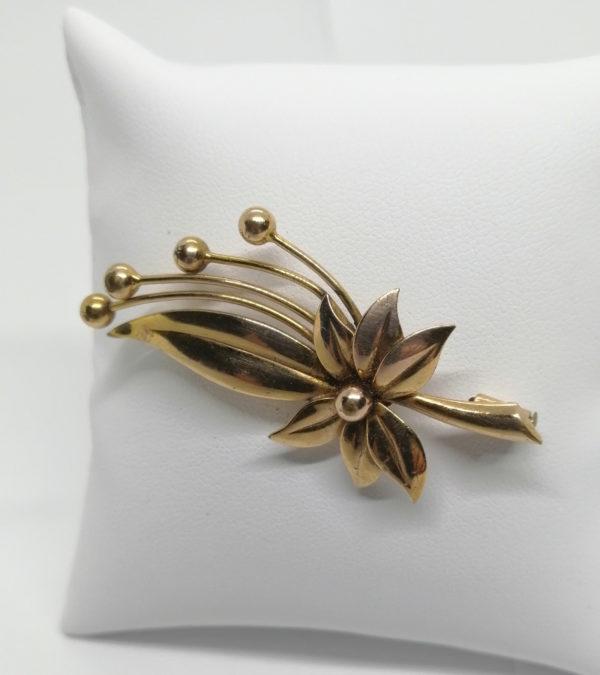 Broche en plaqué or représentant une fleur avec pistil et feuille.