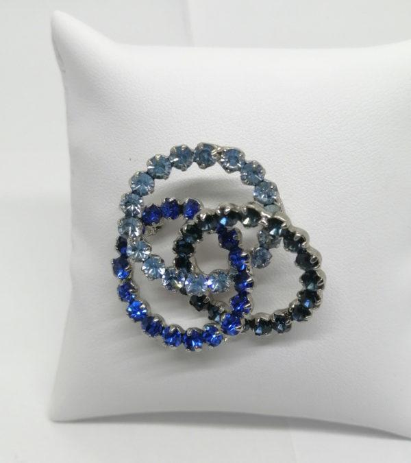 Broche en métal blanc, avec trois anneaux entrelacés et strass bleu.