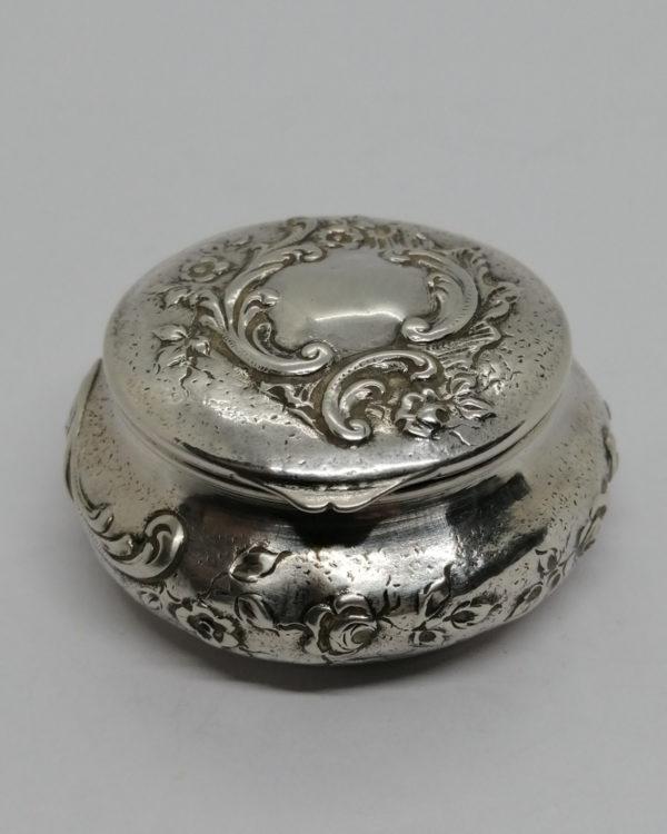 Boîte à pilules en argent massif, sur fond brossé, décor floral et rocaille, vers 1900.